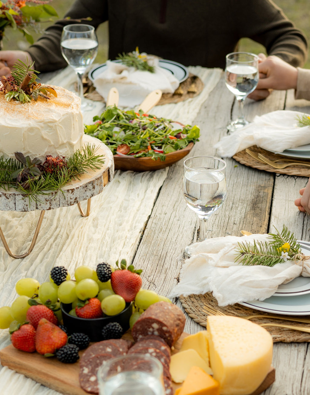 Family gathered around an outdoor table set with bread, salads, fruit and cheese