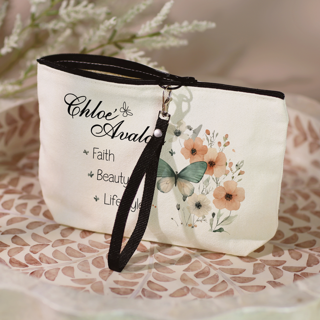 Chloé Avalon cosmetic bag with the butterfly floral design, black zipper and black wristlet lanyard, sitting in a leaf-patterned dish