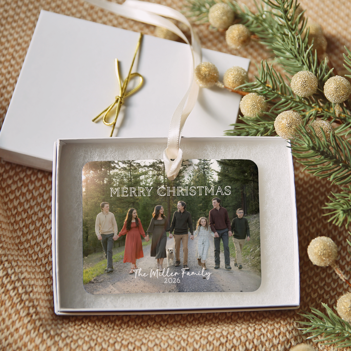 The Miller Family 2026 Christmas ornament resting in its white gift box, with the lid and gold elastic ribbon beside it